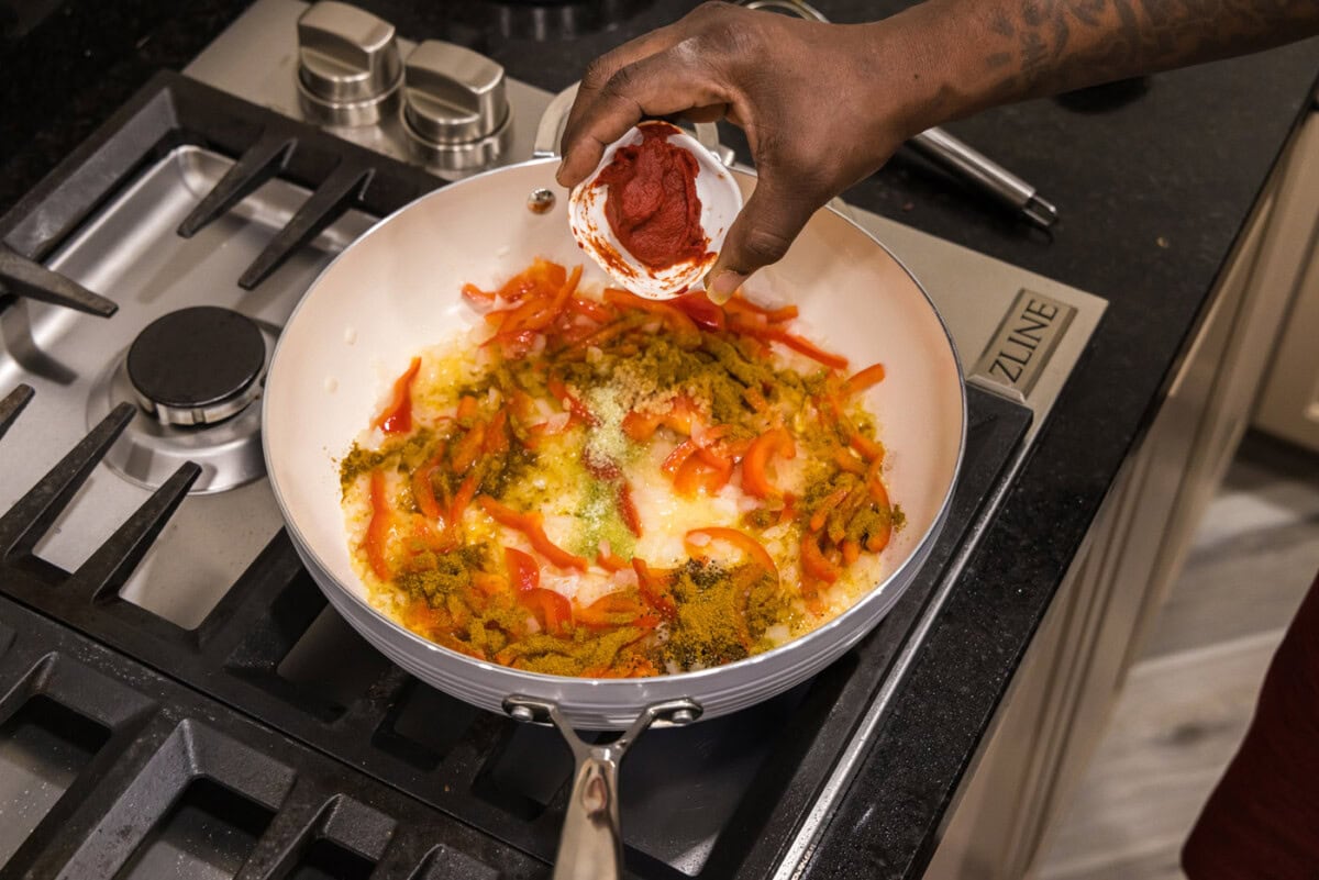 adding tomato paste to skillet with garlic and vegetables