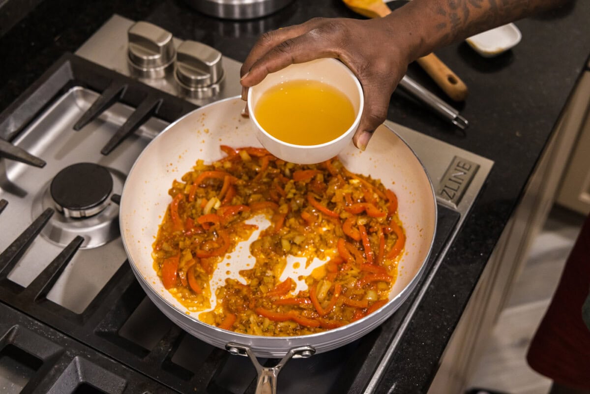 adding chicken stock to curry in a skillet