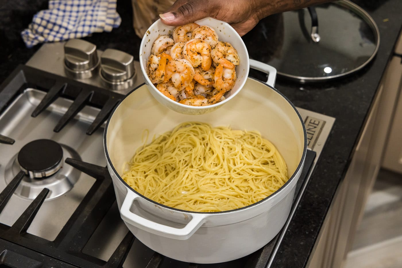 adding shrimp to pasta in a pot