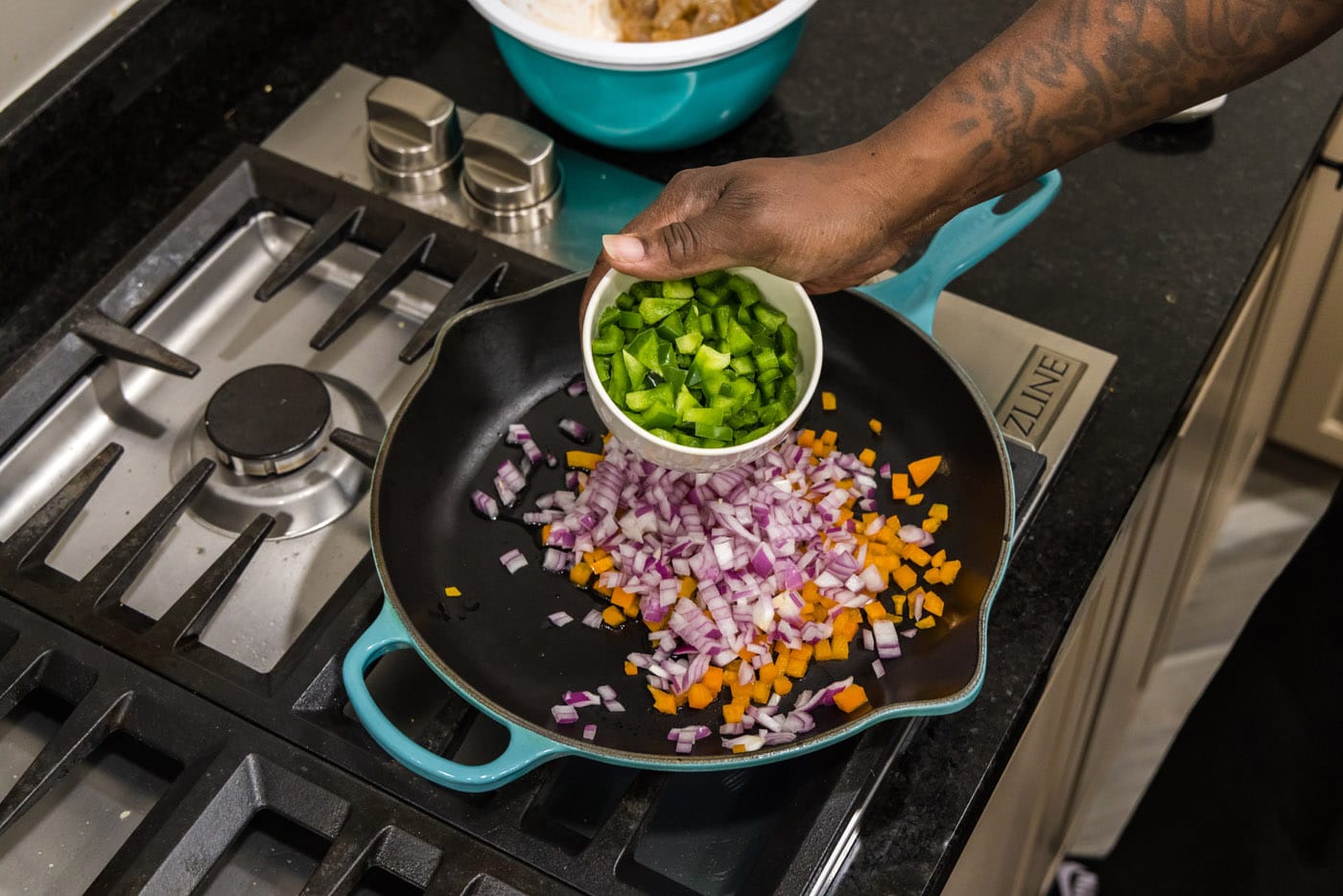 adding green bell pepper to skillet with red onion and orange bell pepper