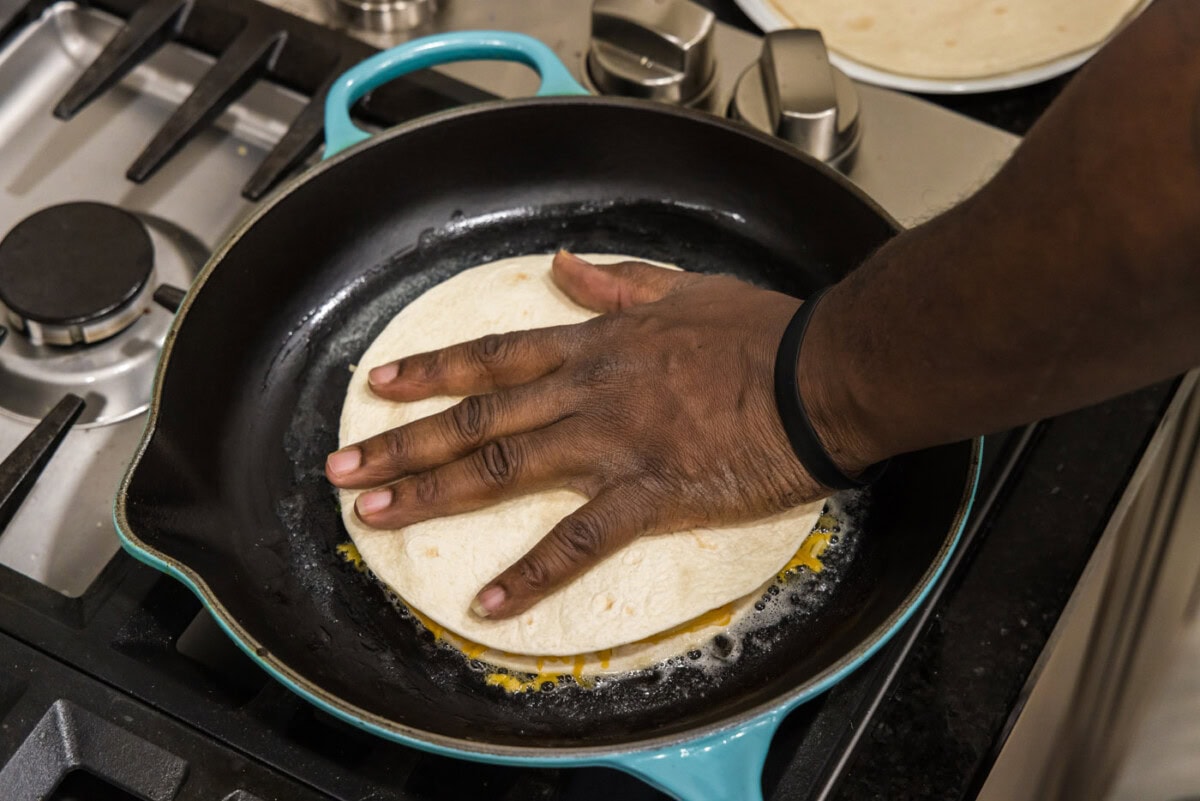 pressing a tortilla on top of cheese, shrimp, and veggies