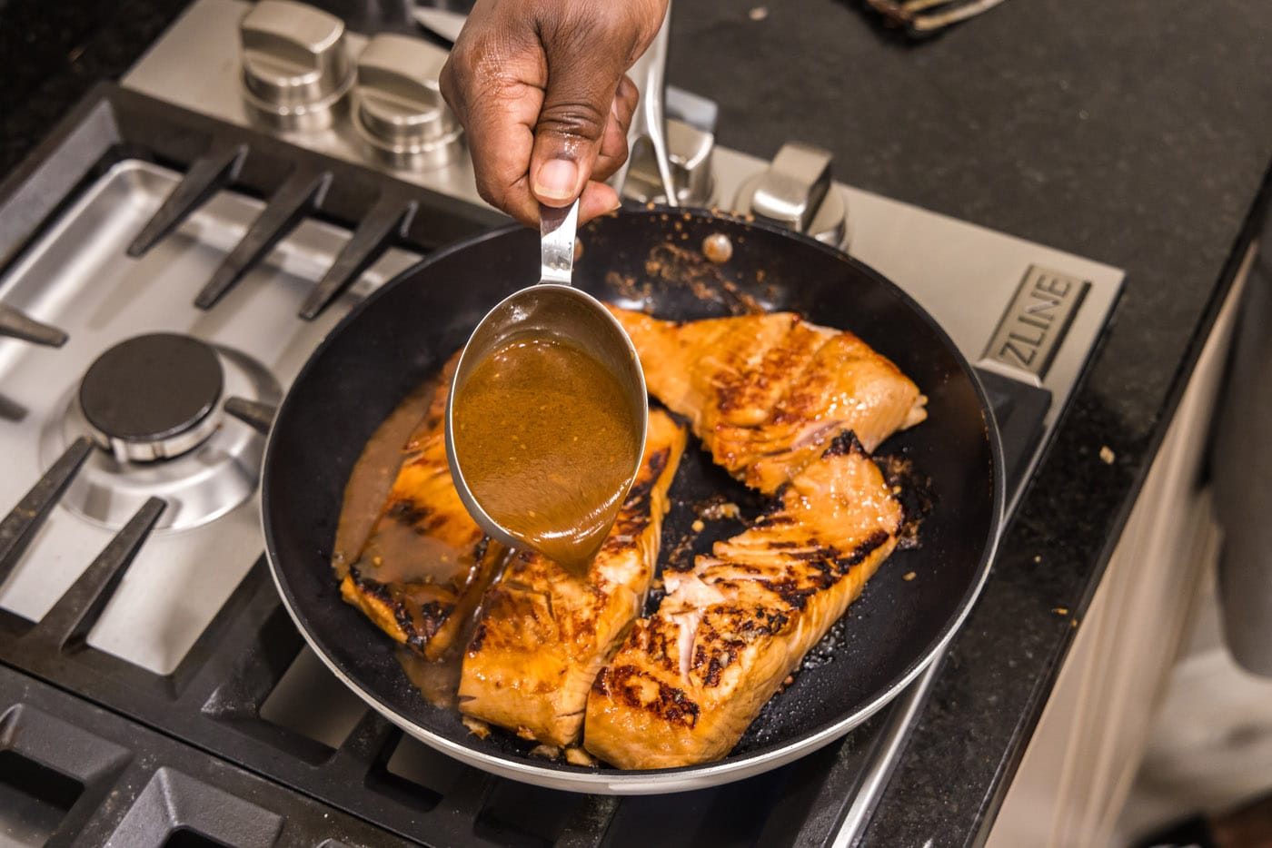 pouring teriyaki sauce into pan with salmon