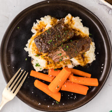 Overhead photo of Boneless Beef Short Ribs served on mashed potatoes with carrots on the side