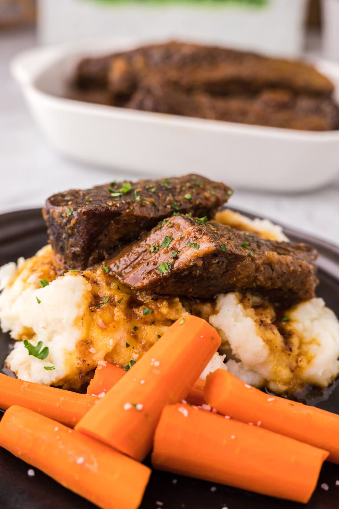 Boneless Beef Short Ribs on a bed on mashed potatoes with carrots on the side