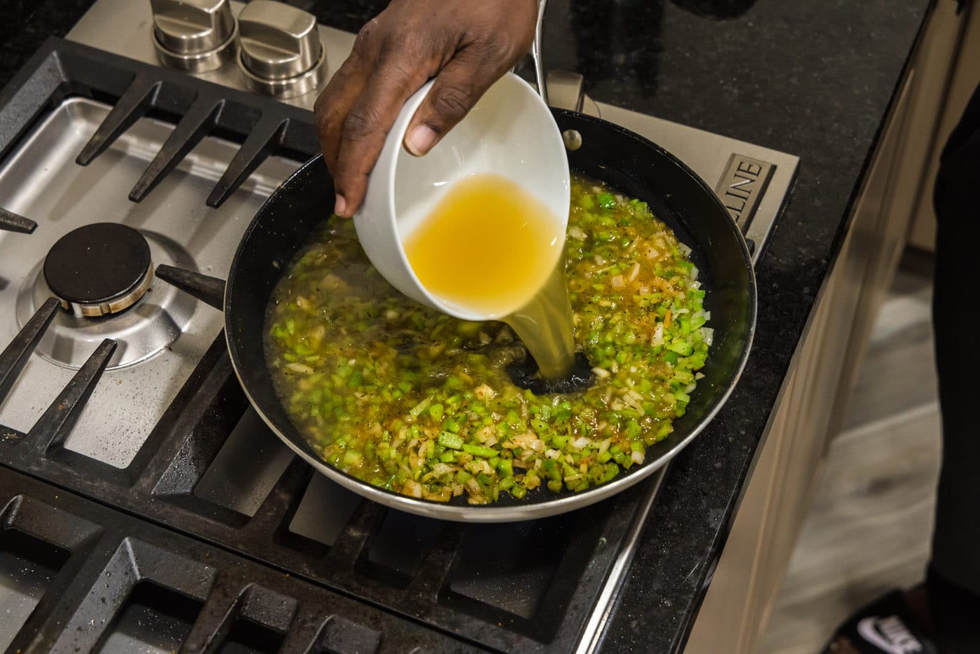 pouring chicken stock into skillet with celery, green pepper, and onion