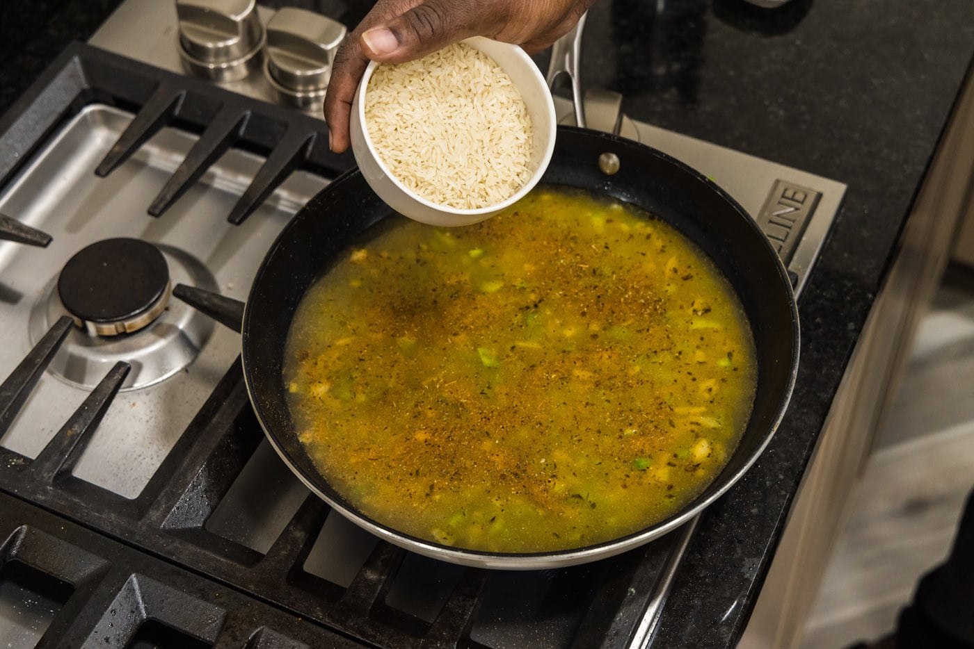 pouring Basmati rice into skillet with chicken stock and vegetables