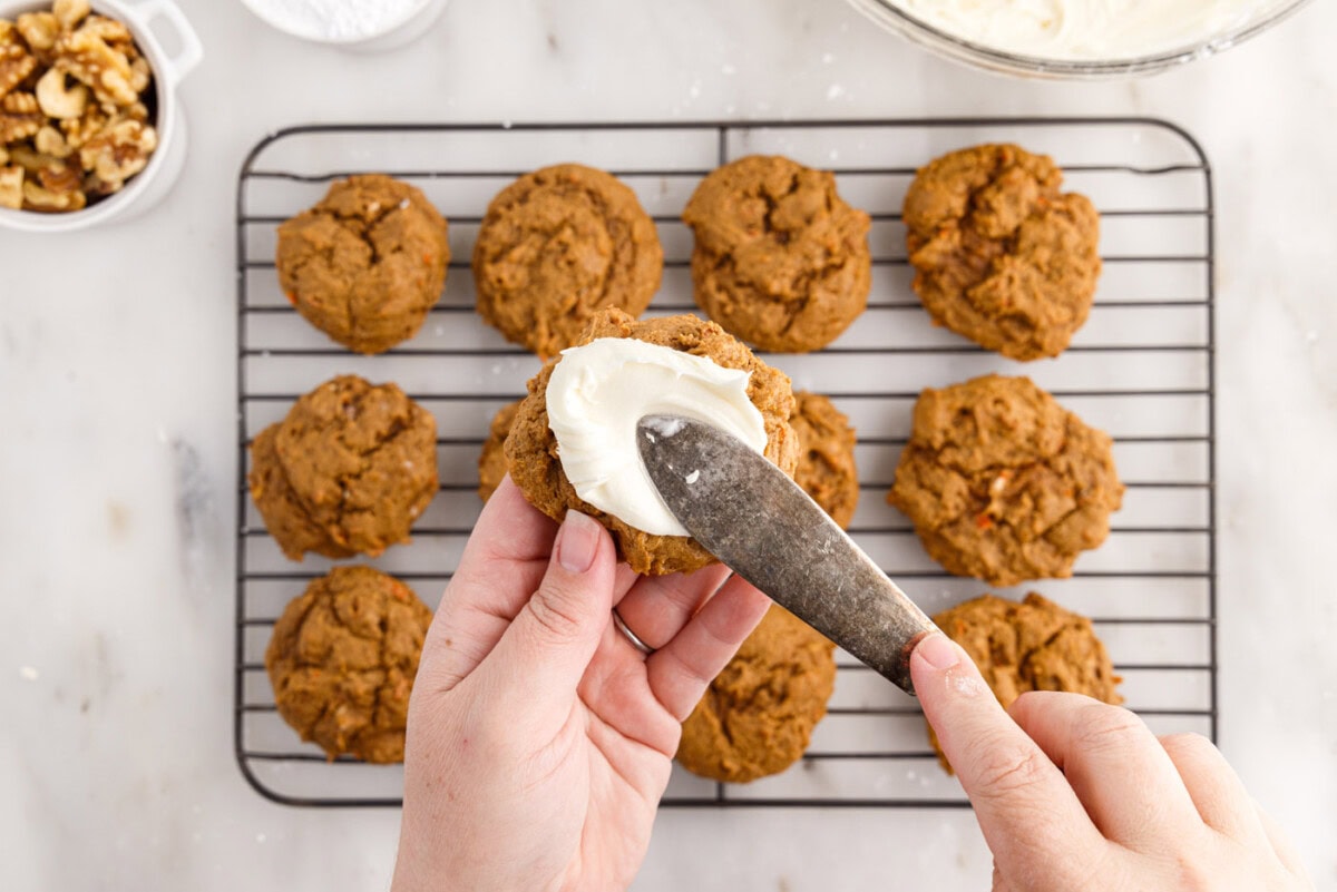 spatula smearing frosting onto carrot cake cookies