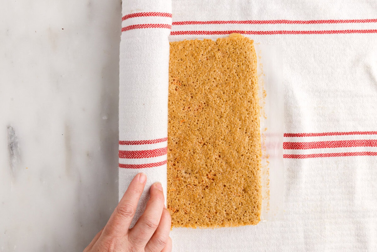 rolling carrot cake into a log with a tea towel