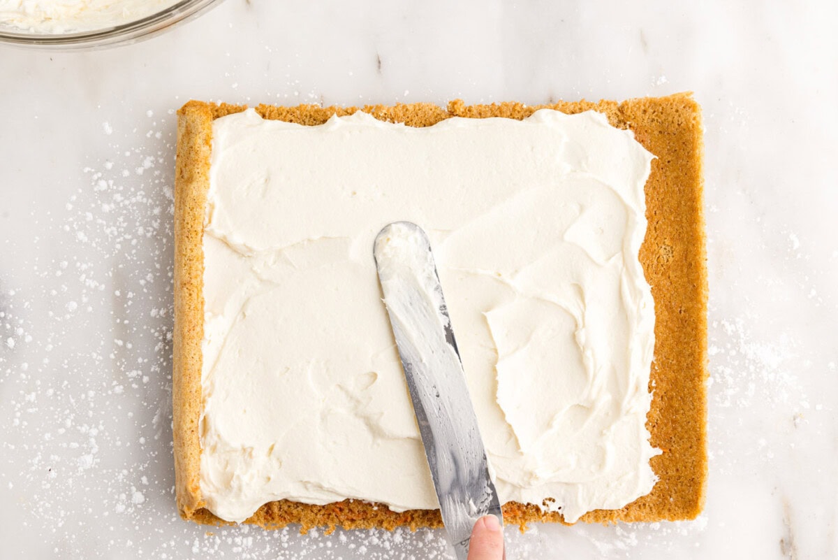 spreading cream cheese filling on top of carrot cake
