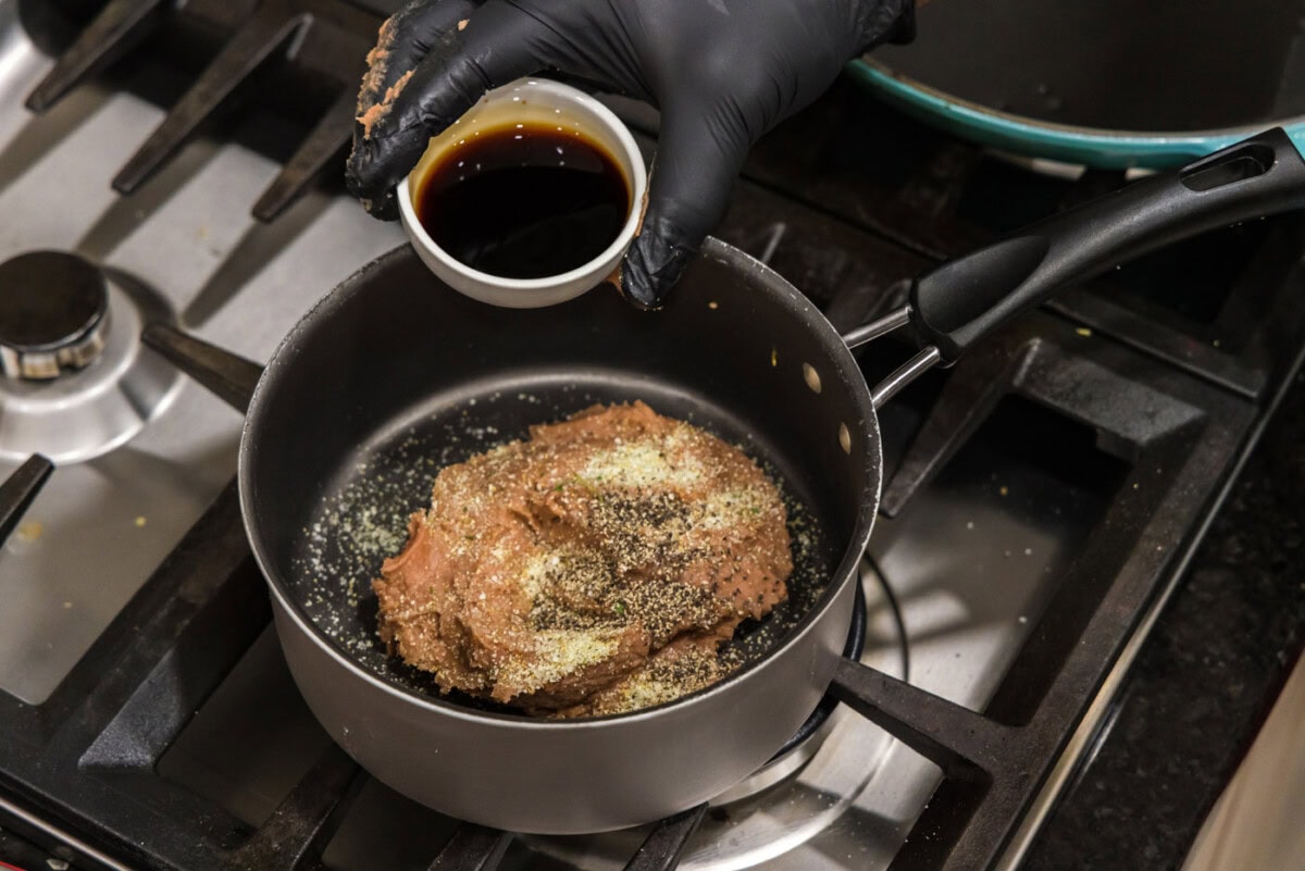 adding soy sauce to refried beans in a saucepan with seasonings