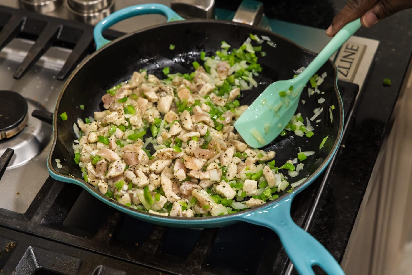 mixing vegetables with chicken in a skillet