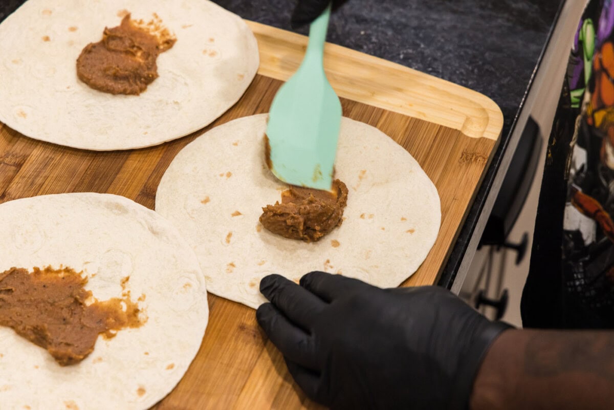 spatula spreading refried beans onto taco shell
