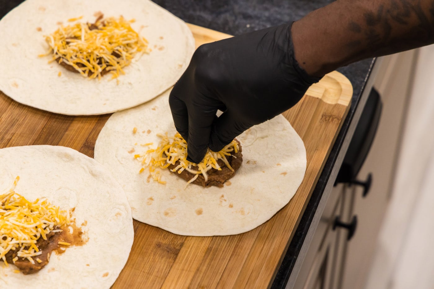 adding shredded cheese on top of refried beans on a tortilla shell