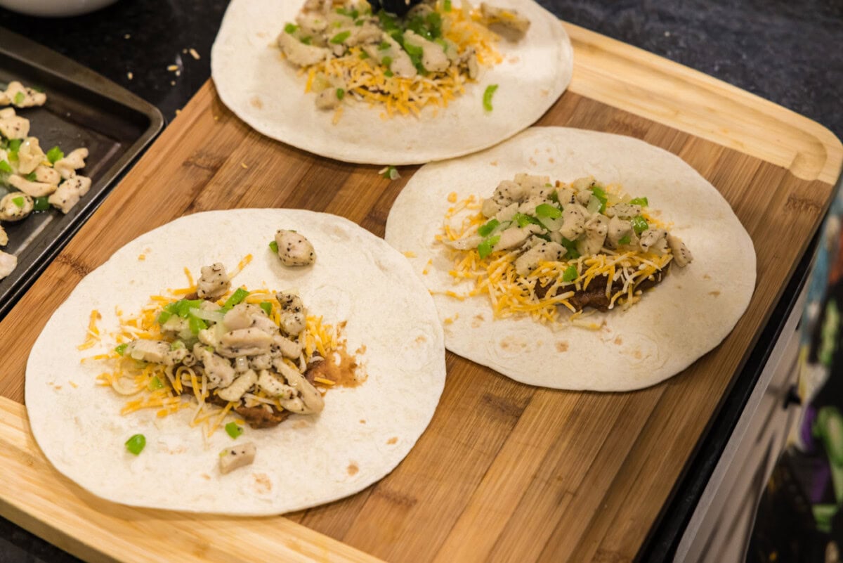 vegetables added to cheese, beans, and chicken on a tortilla