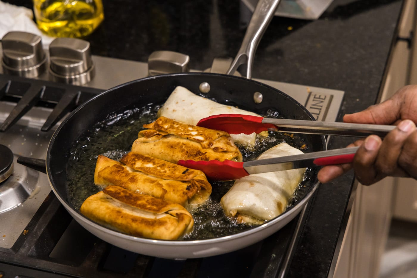 tongs flipping chimichangas in oil