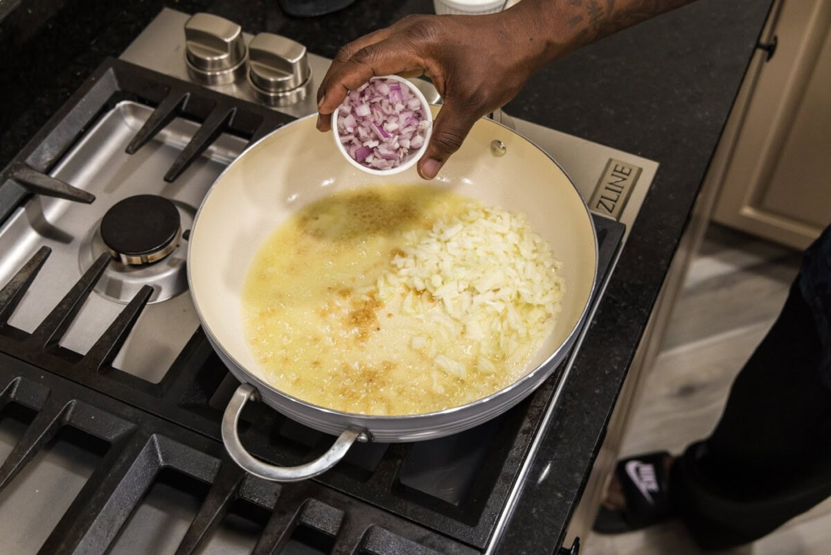 adding shallots to skillet with onion and garlic with oil