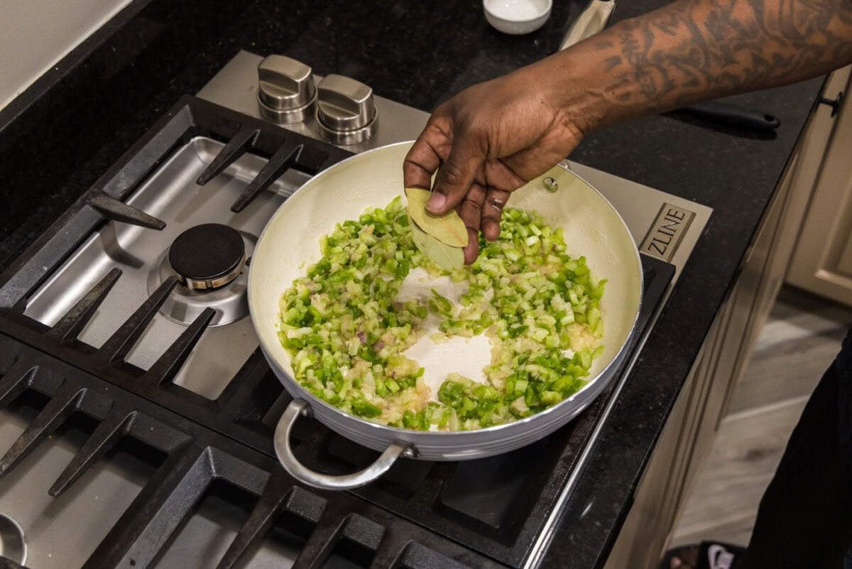 adding bay leaves to skillet of onion, bell pepper, and celery