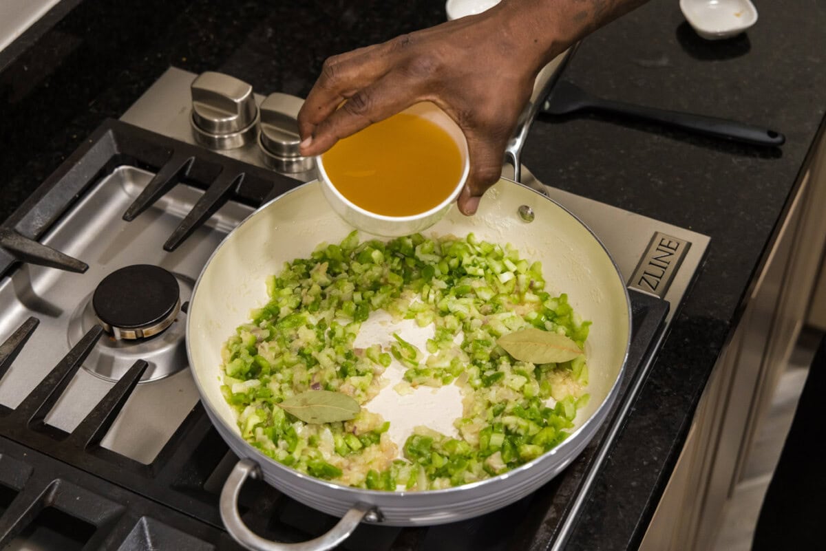 adding chicken stock to skillet of holy trinity vegetables