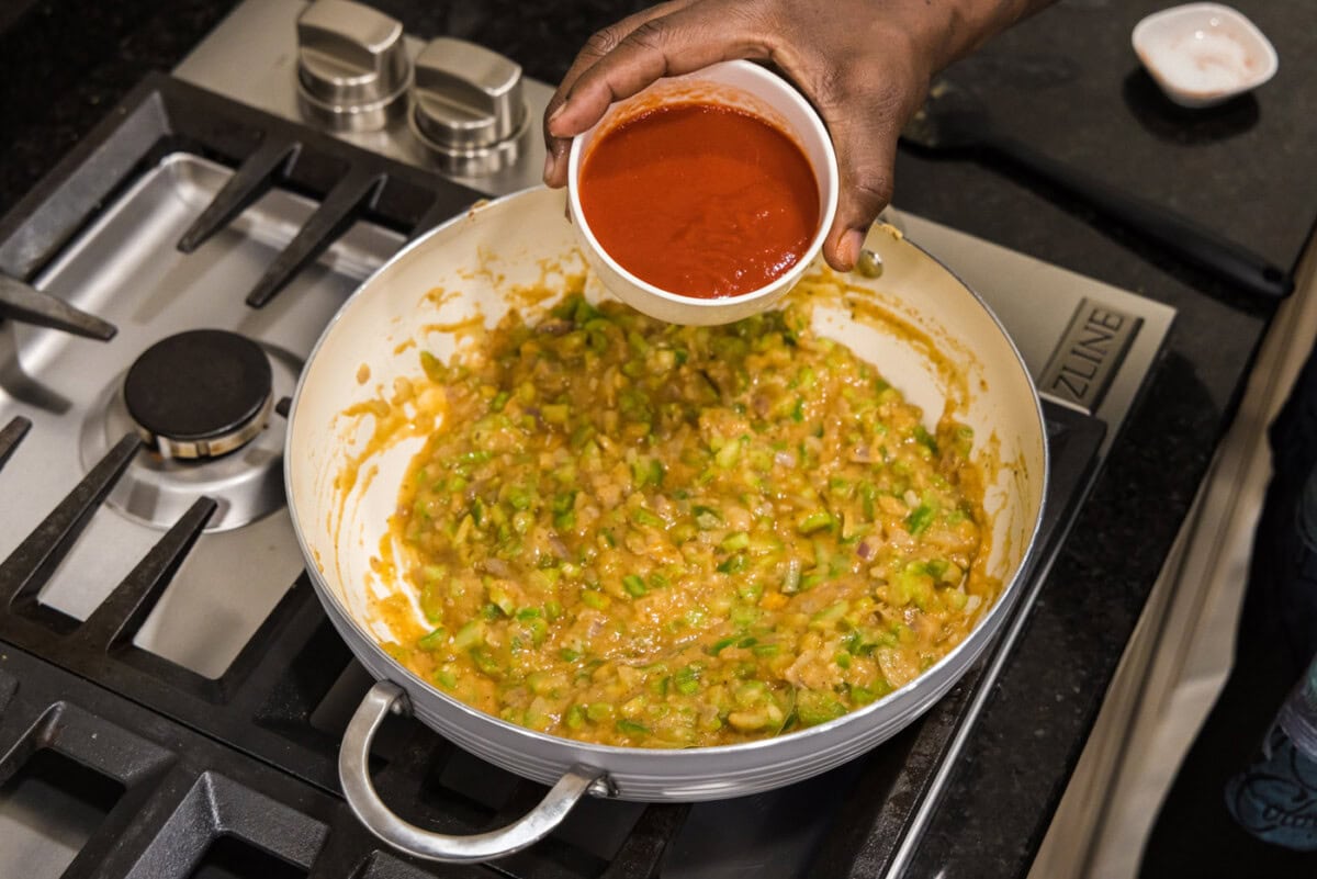 pouring tomato sauce into skillet with vegetable roux