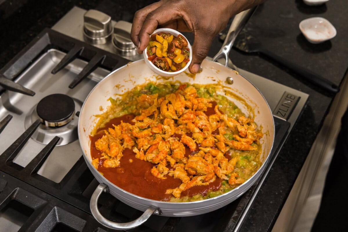 adding cherry tomatoes to crawfish etouffee in a skillet