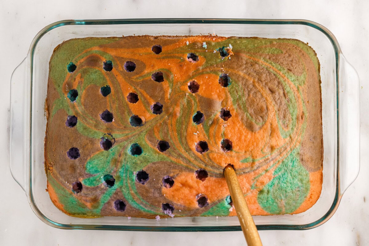 poking the top of a cake with a wooden spoon