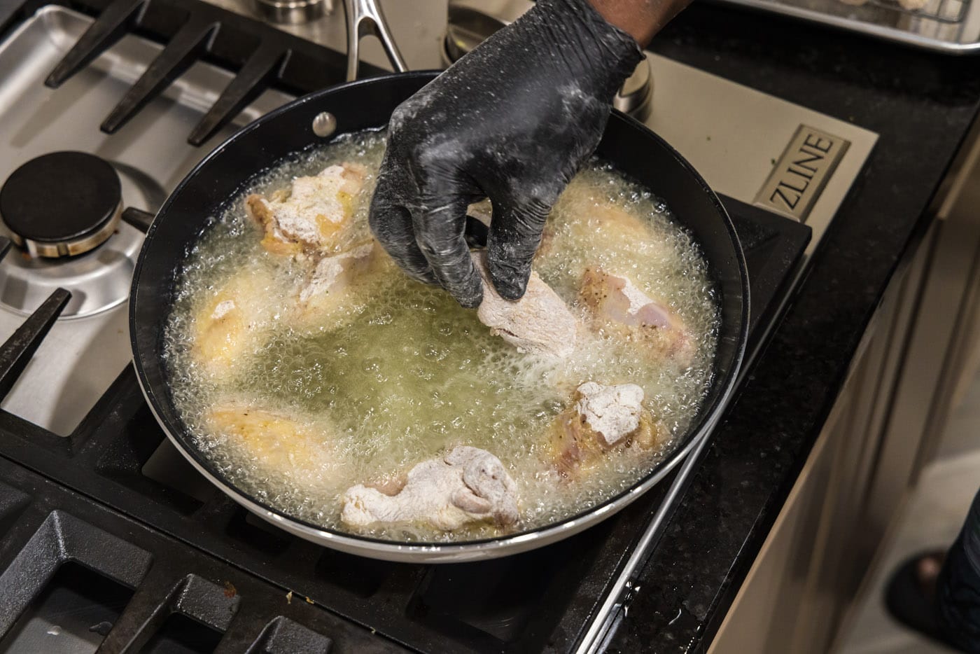 adding chicken wings to hot oil in a skillet