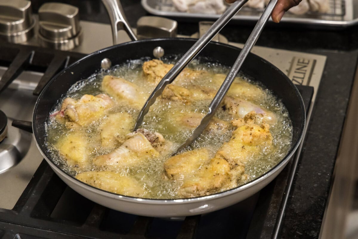 tongs flipping chicken wings in a skillet