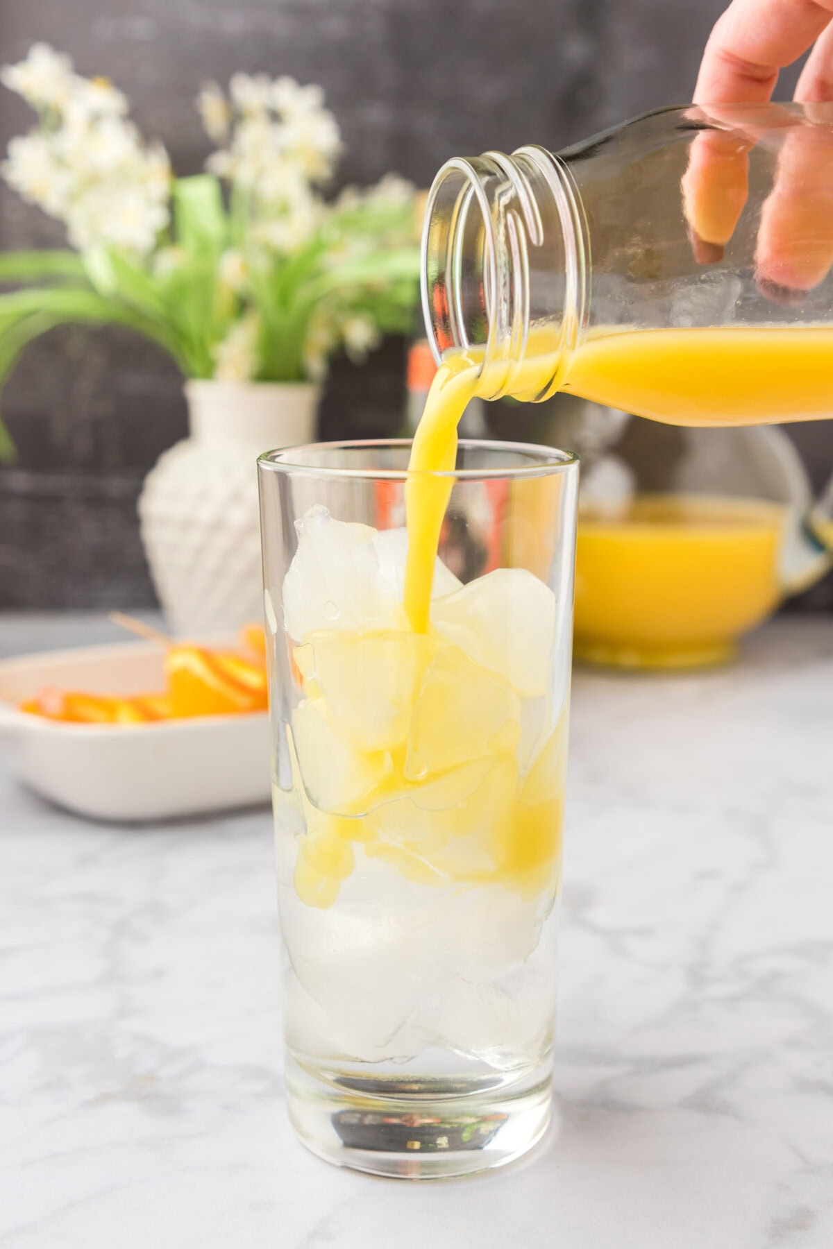 pouring orange juice into glass of peach schnapps and ice
