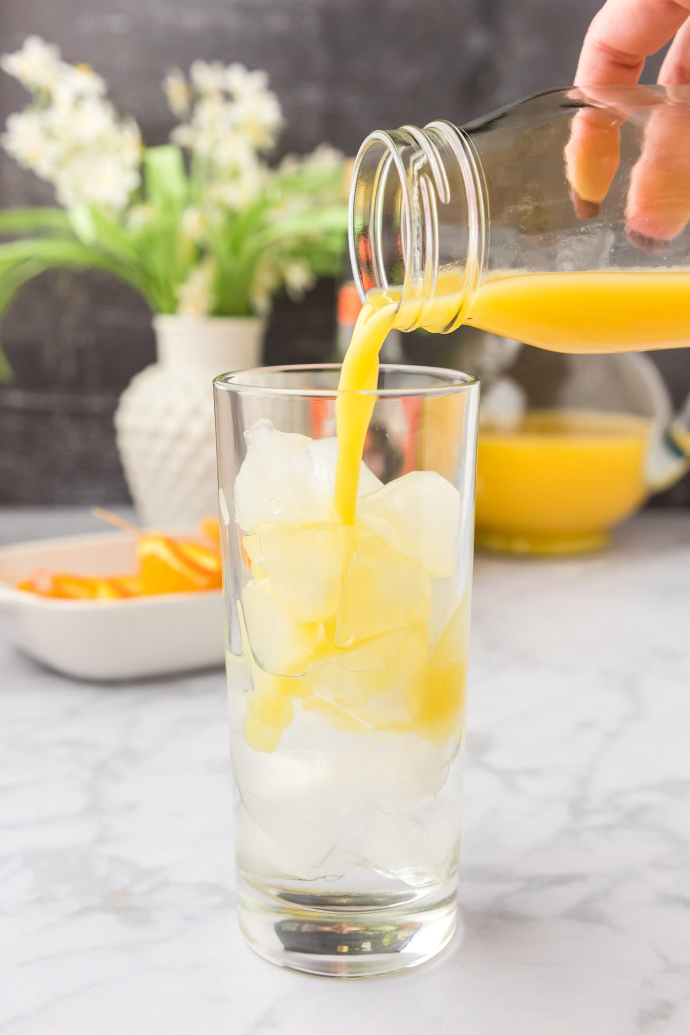 pouring orange juice into glass of peach schnapps and ice