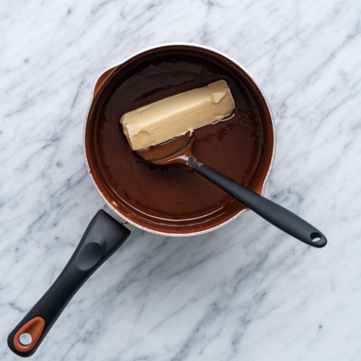 adding butter to hot fudge in a pot