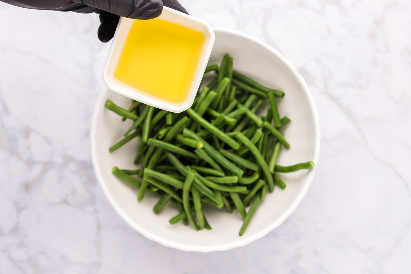 adding olive oil to green beans in a bowl