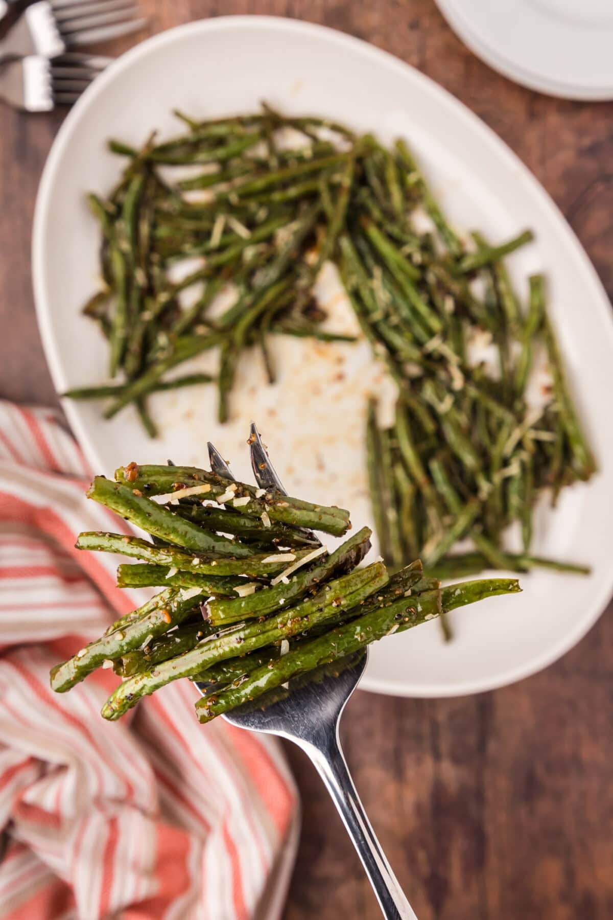 Serving fork full of Roasted Green Beans held above a platter of Roasted Green Beans