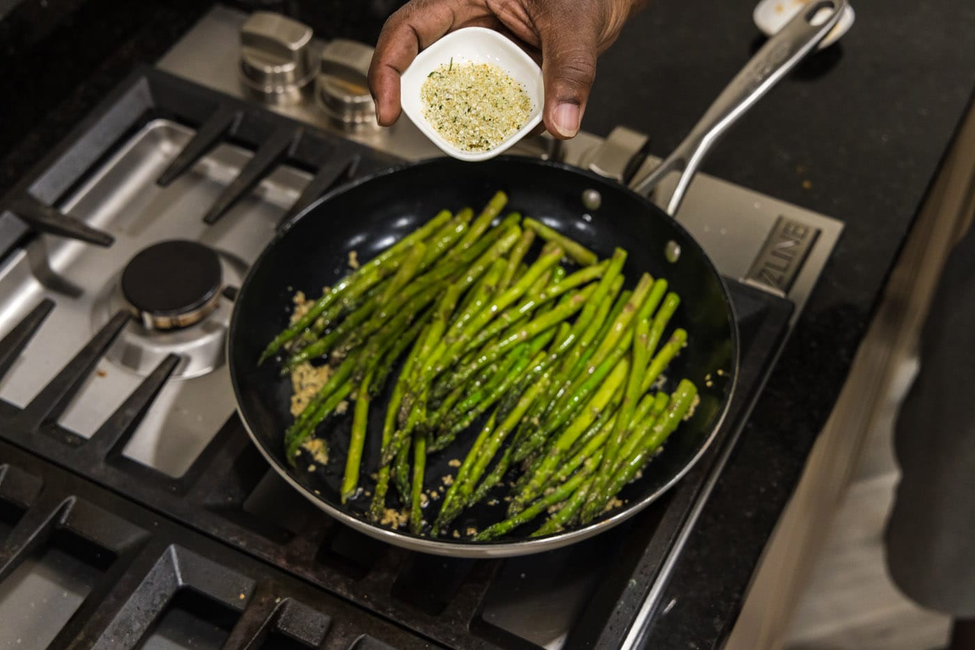 adding garlic salt to asparagus in a pan