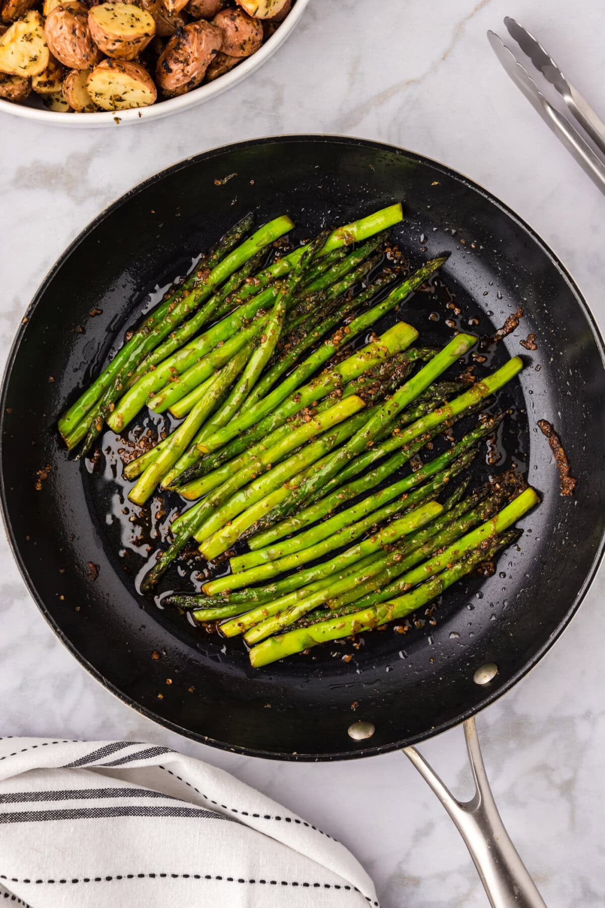 Sautéed Asparagus in a skillet with roasted red potatoes in the background