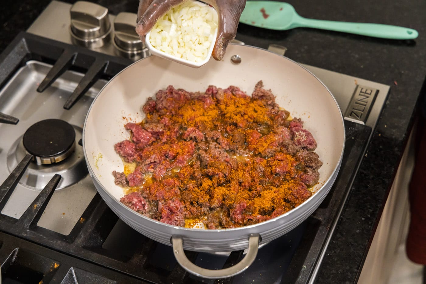 adding chopped onion to skillet with ground beef