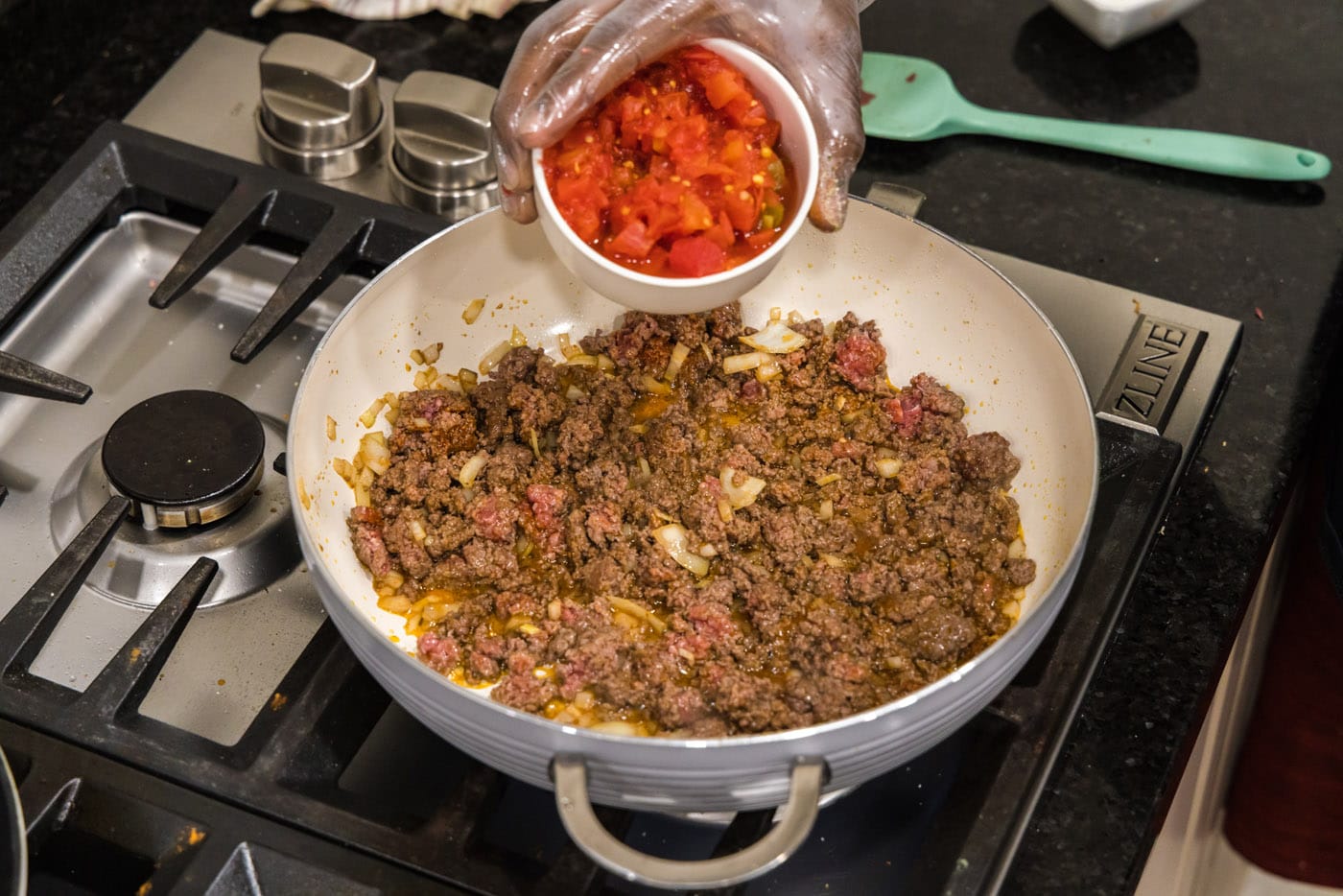 adding Rotel tomatoes to skillet with ground beef and onion