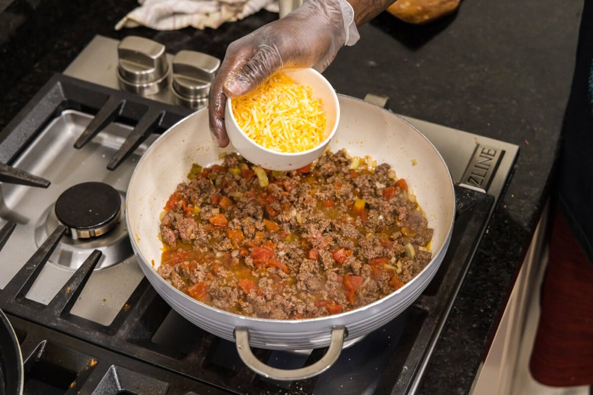adding cheese to skillet with ground beef, onion, and tomatoes