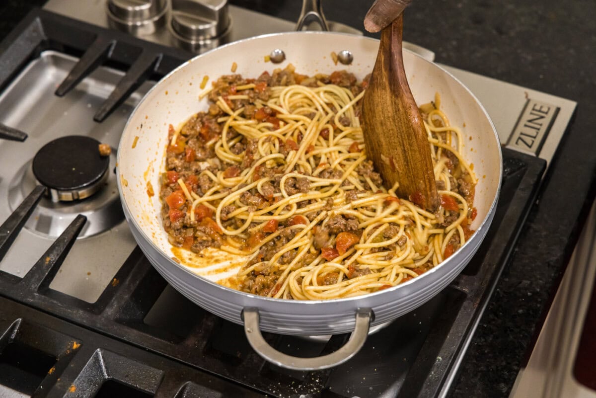 mixing spaghetti into taco seasoned ground beef with tomatoes and onion
