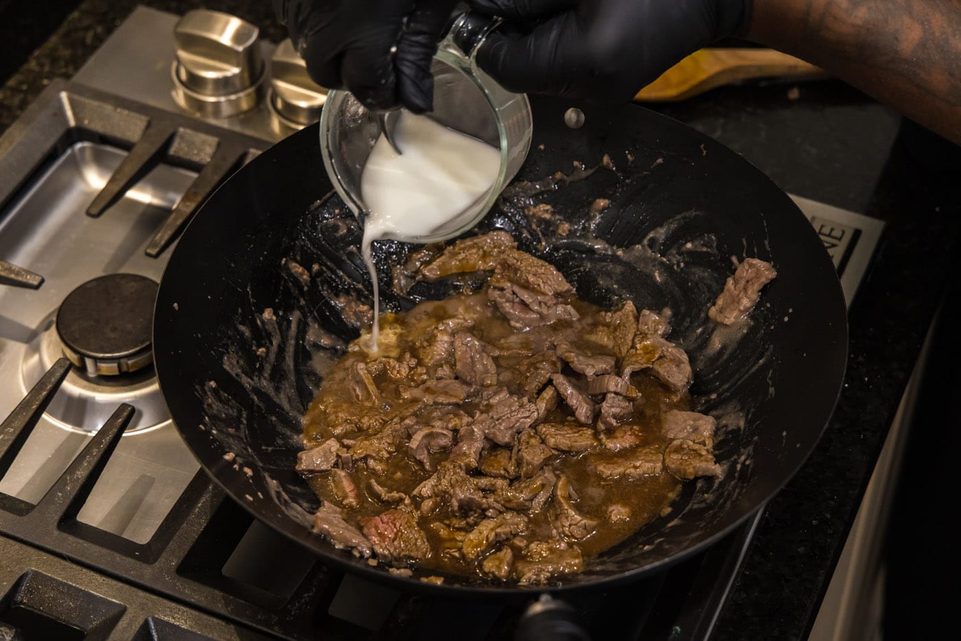 adding cornstarch water to skillet with beef strips and teriyaki sauce