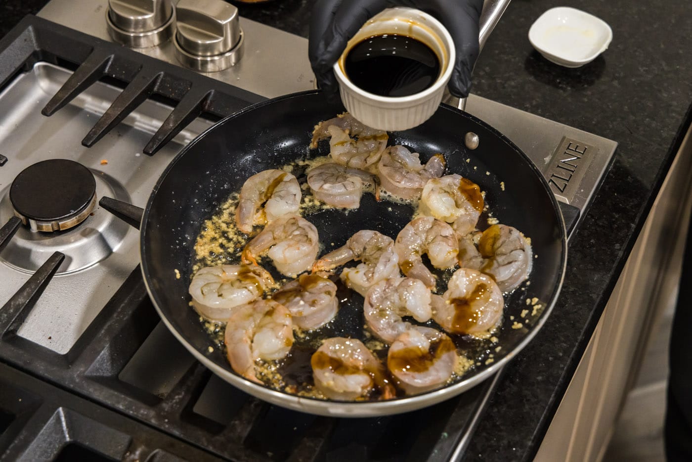 pouring soy sauce into skillet with sesame oil, oyster sauce and shrimp