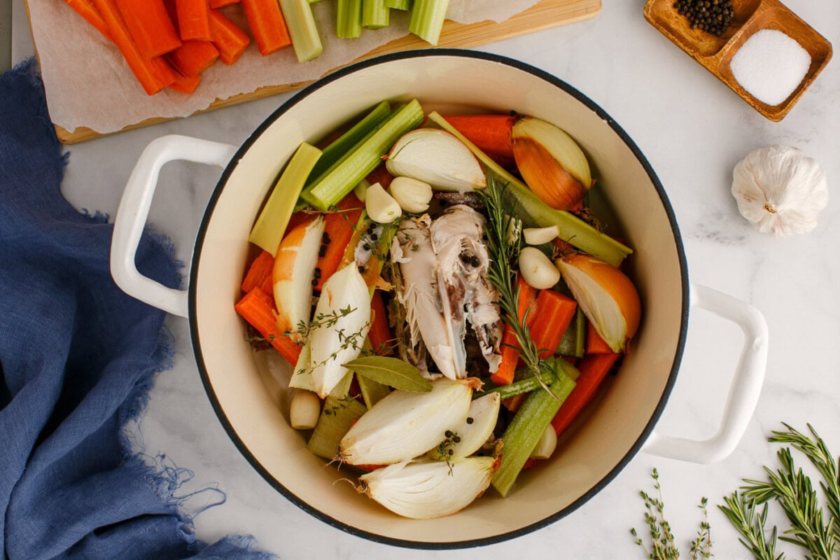 adding herbs to homemade chicken stock in a pot