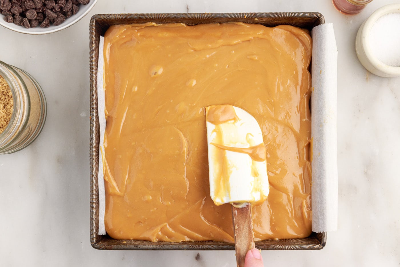 rubber spatula spreading caramel over shortbread crust