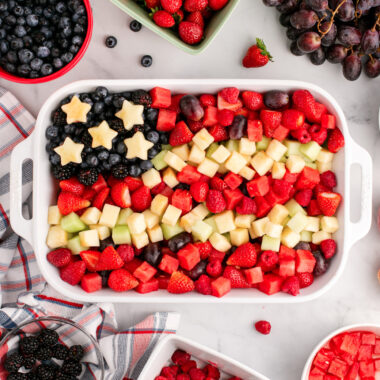 Red White & Blue Fruit Salad in a white serving dish surrounded by fruit