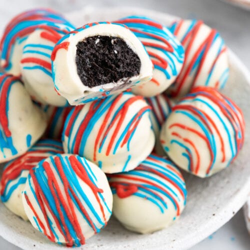 Red White and Blue Oreo Truffle with a bite taken out resting on top of a bunch of Red White and Blue Oreo Truffles in a bowl