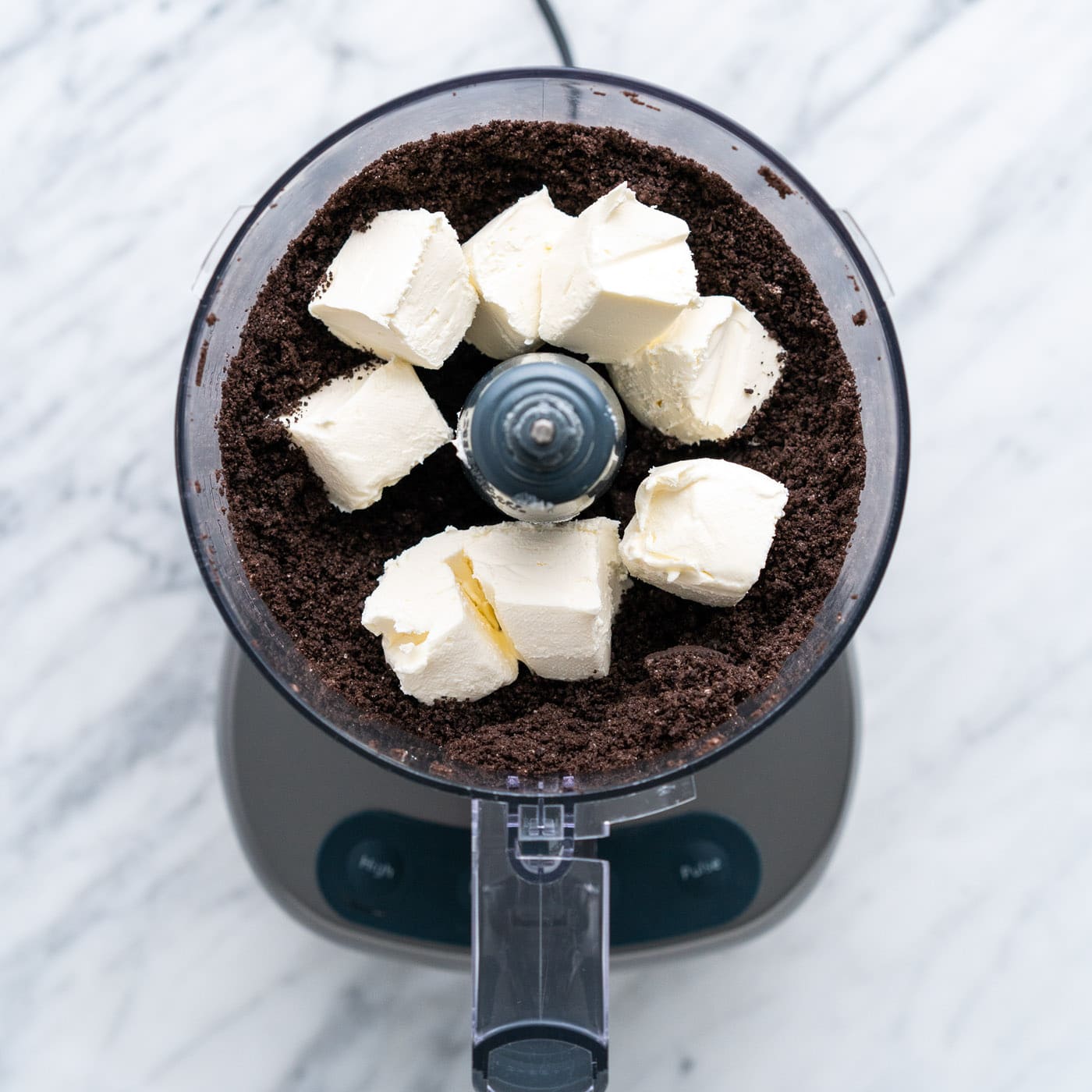 cubed cream cheese added to food processor with oreos