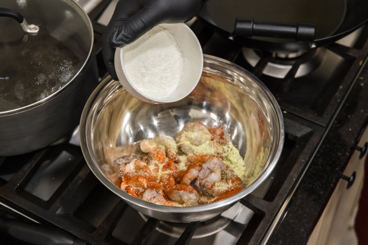 adding cornstarch to seasoned shrimp in a bowl