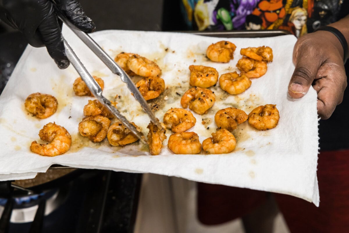 tongs transferring fried shrimp to paper towels