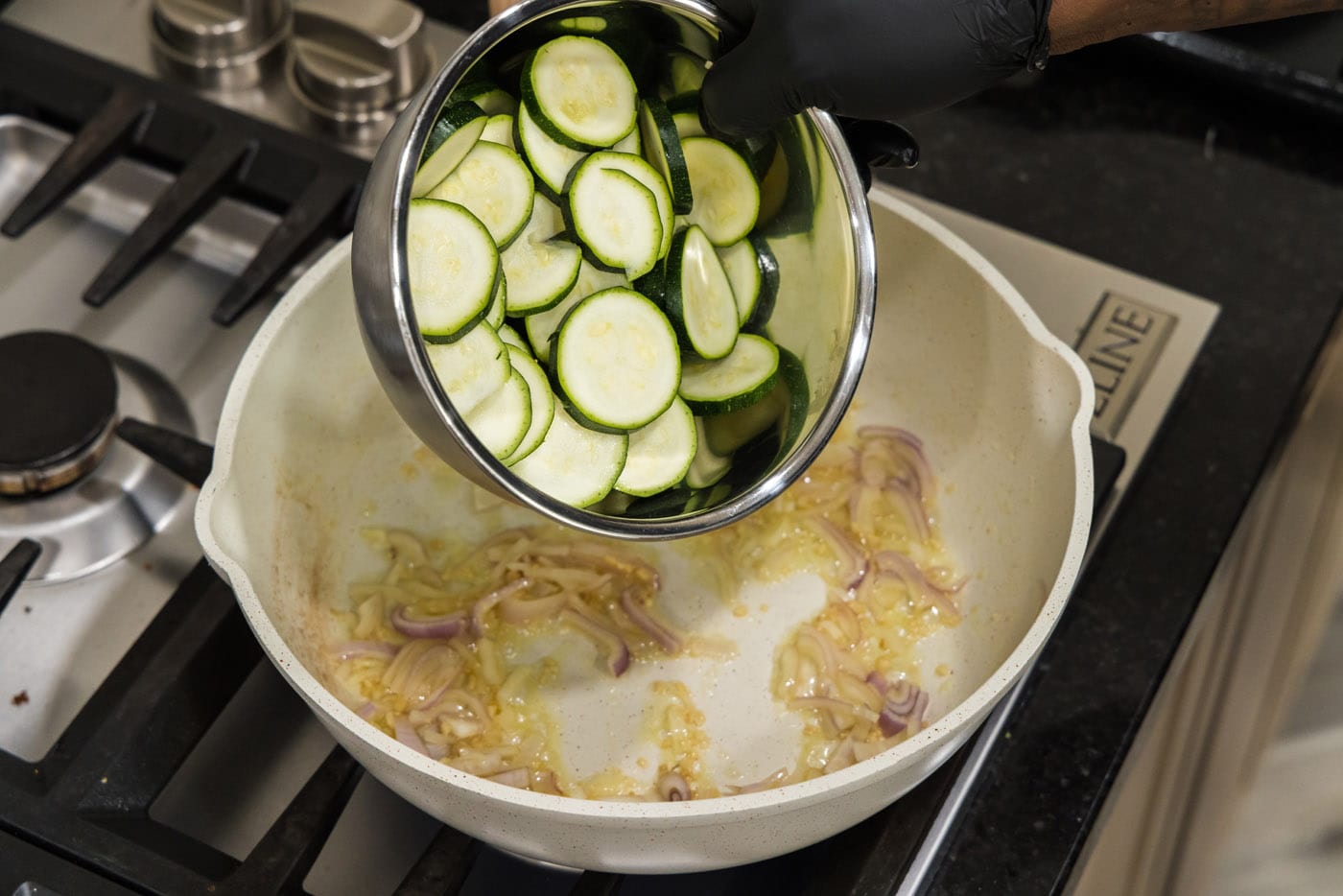 pouring sliced zucchini into a skillet with shallots, garlic, and butter