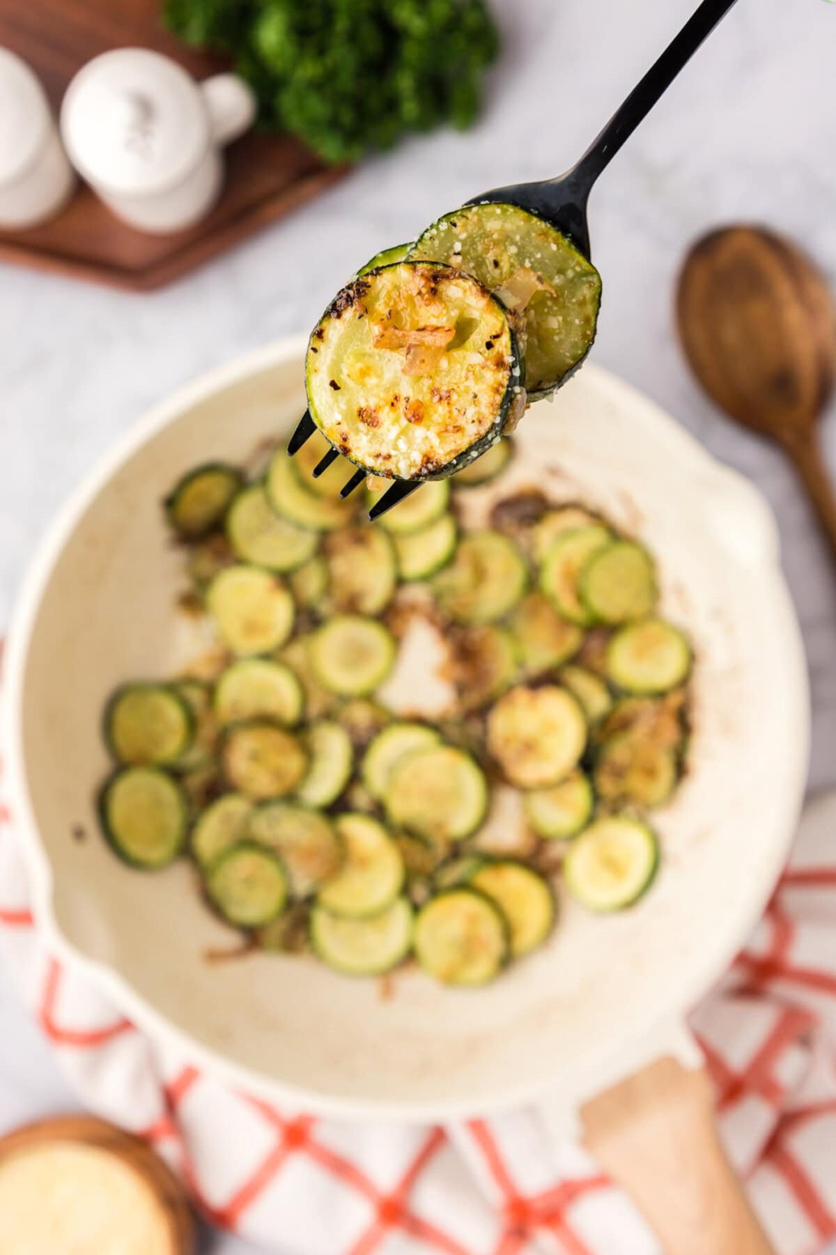 Sautéed Zucchini on a fork held above a skillet of Sautéed Zucchini