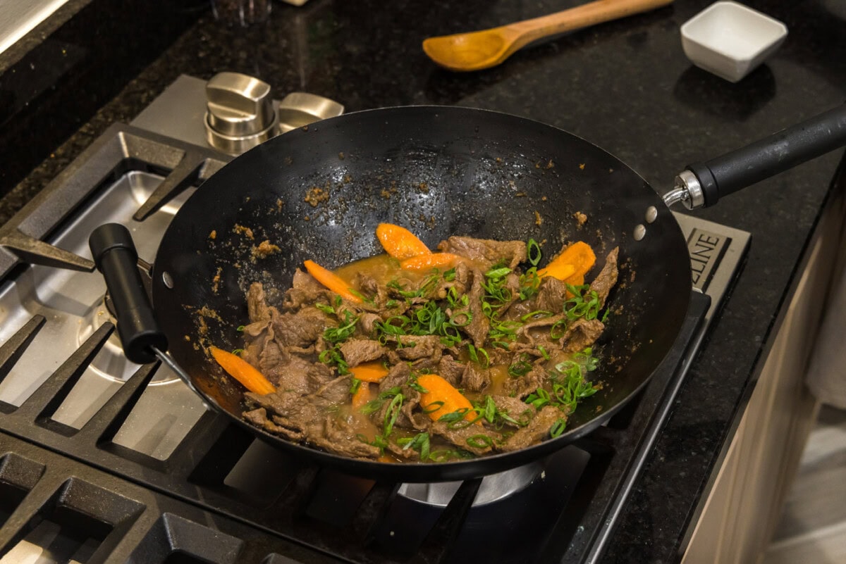 beef, sliced carrots, and green onions in a wok